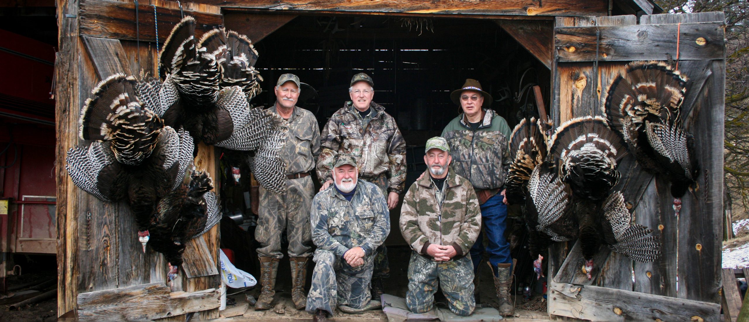 five hunters posing with five wild turkeys on barn doors