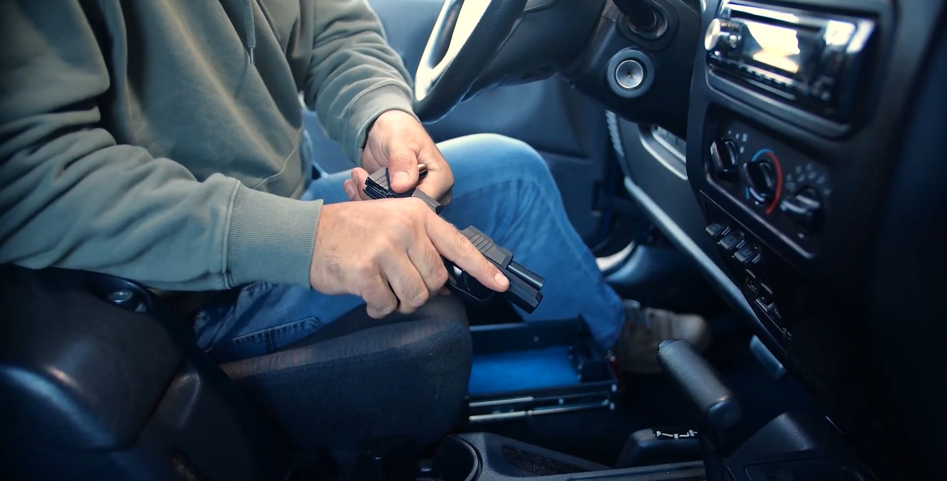 Driver holding a firearm and getting ready to place it in an under the seat gun safe