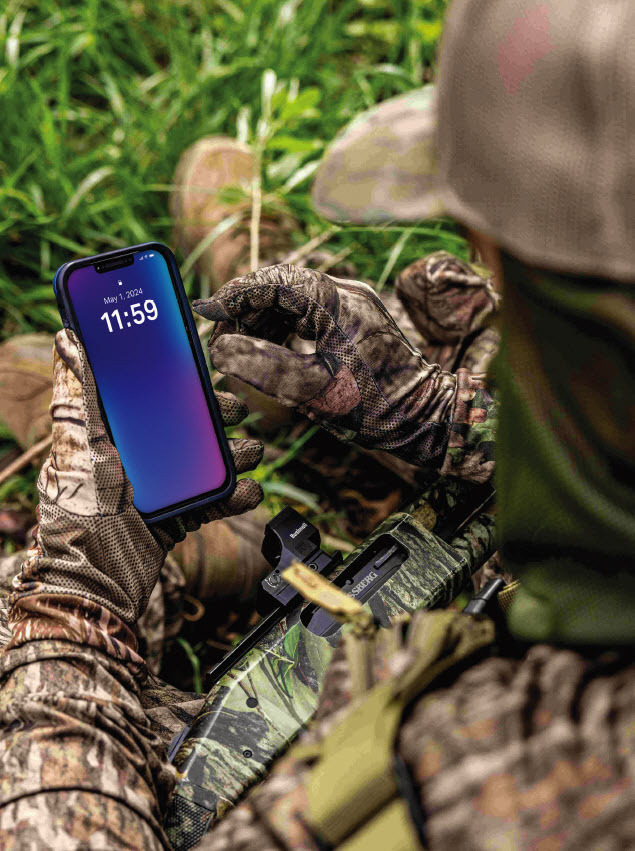 A hunter looks at his phone, which says it is 11:59 am.