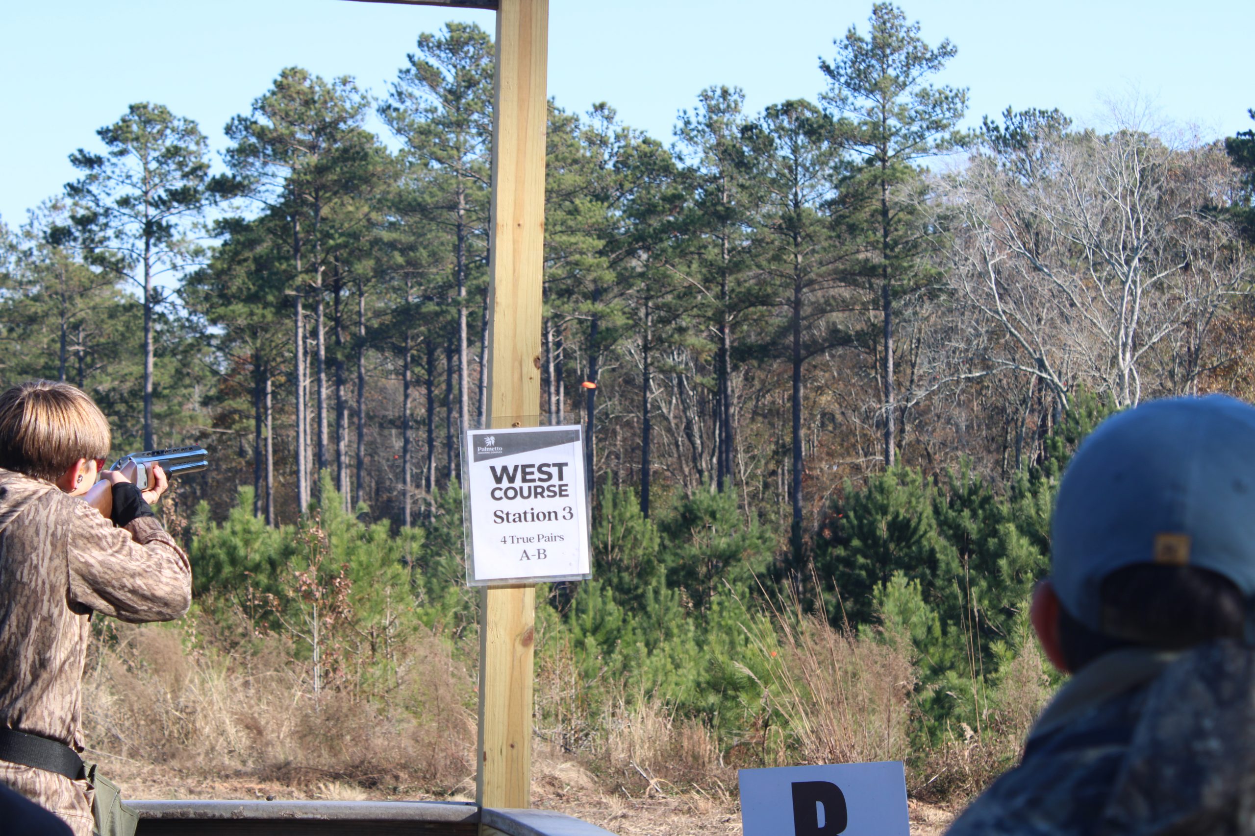 A youth shooting takes aim at a flying clay target.